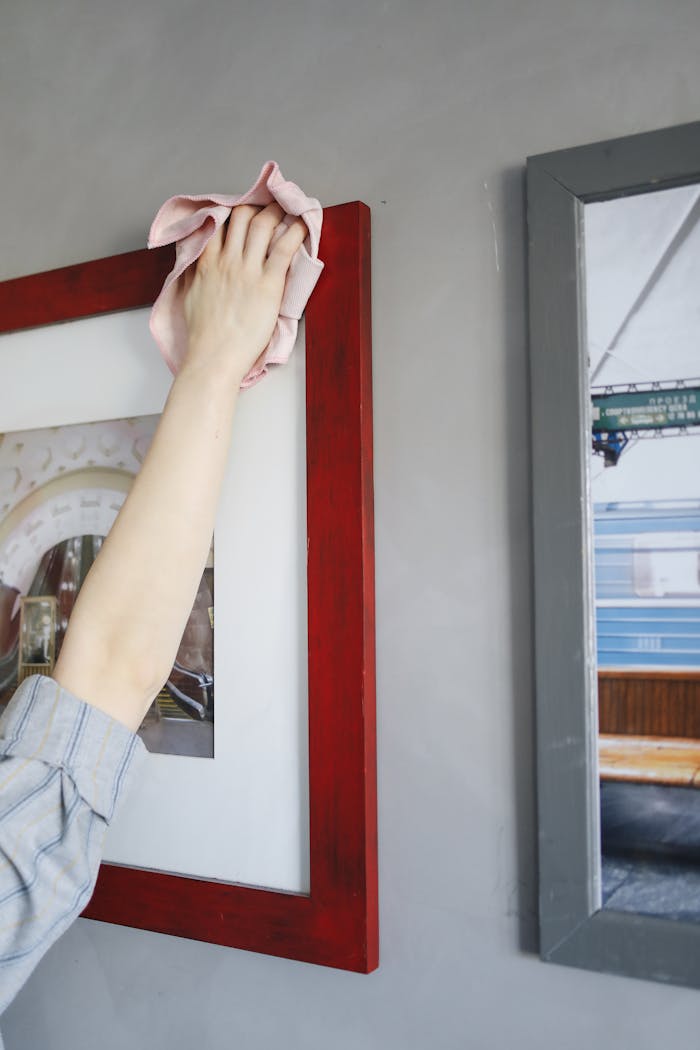 A person's hand cleaning a red picture frame in a well-lit indoor environment.