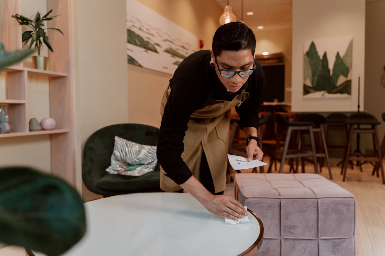 A barista wipes down a table in a stylish café interior, showcasing cleanliness and hospitality.
