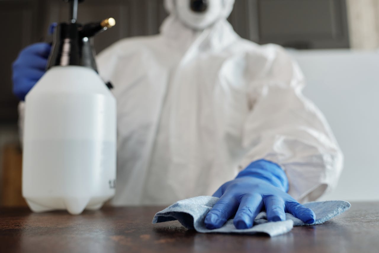 Close-up of a person in protective gear disinfecting a surface, emphasizing hygiene and cleanliness.