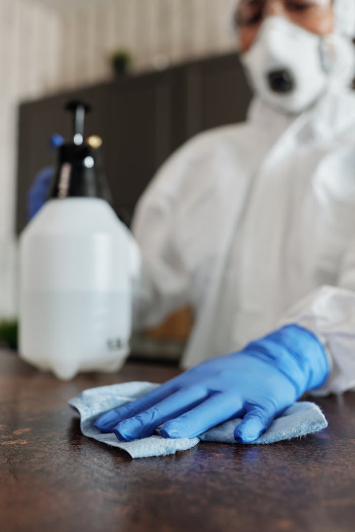 Close-up of a professional in full protective gear disinfecting a surface indoors.